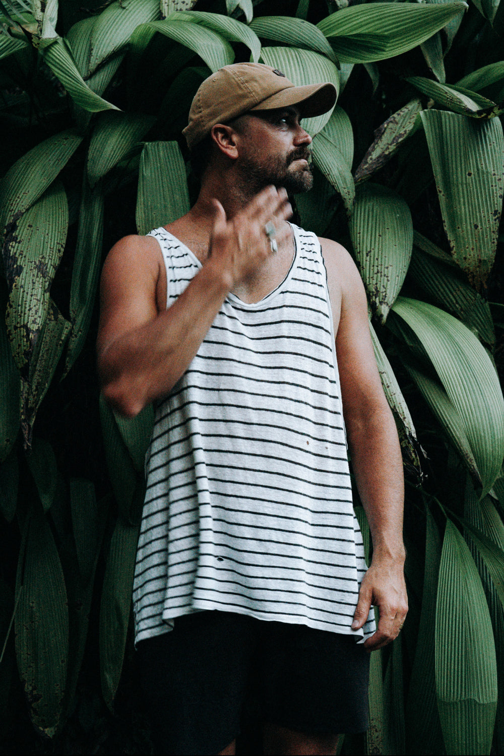 Man wearing a striped tank top and cap standing in front of green foliage