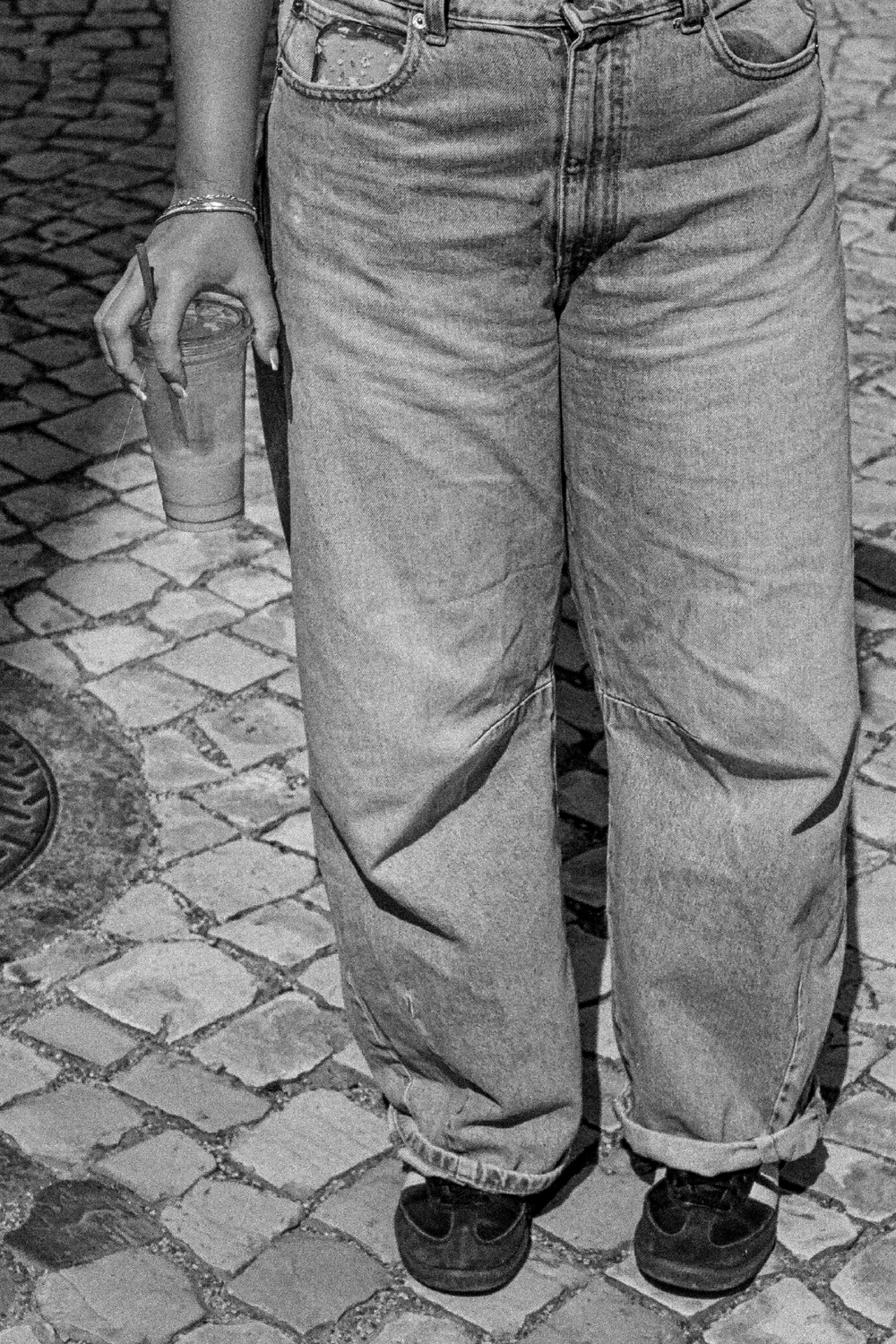 Person wearing jeans standing on a cobblestone street drink soak coffee iced latte
